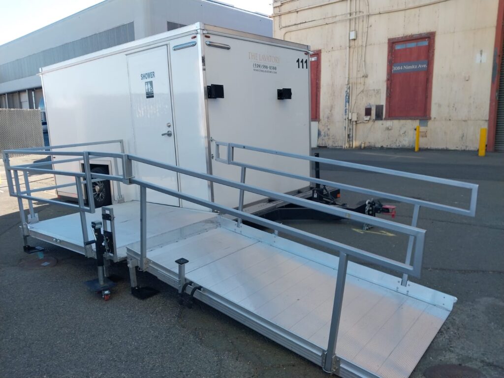 Fold-out aluminum ramp and platform rails on an ADA plus 2 shower trailer in a paved yard, The Lavatory Los Angeles