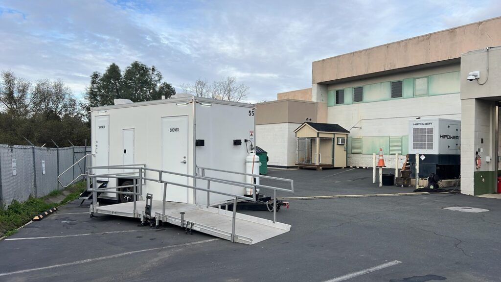 ADA plus 2 shower trailer with its ramp set up in a paved lot beside an office building, The Lavatory Los Angeles