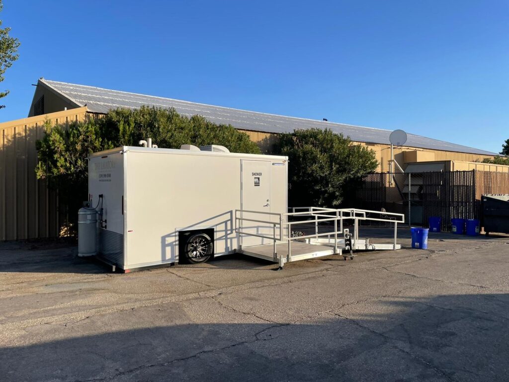 ADA plus 2 shower trailer with a propane tank and railed platform in a production yard beside a warehouse, The Lavatory Los Angeles