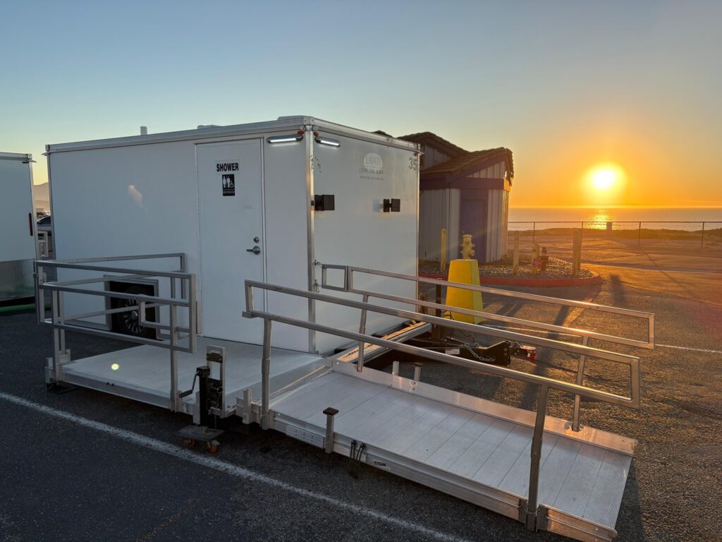 ADA plus 2 shower trailer with a railed wheelchair ramp and platform in a seaside parking lot at sunset, The Lavatory Los Angeles
