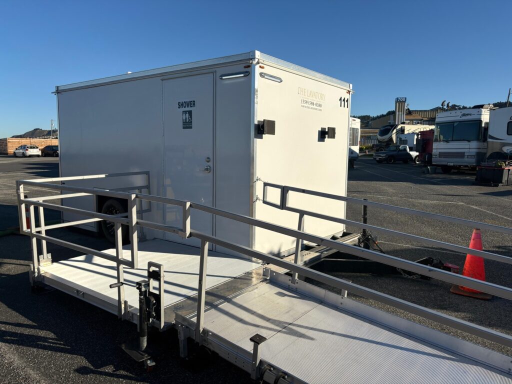 ADA plus 2 shower trailer with a railed platform and a safety cone in a parking lot lined with RVs, The Lavatory Los Angeles