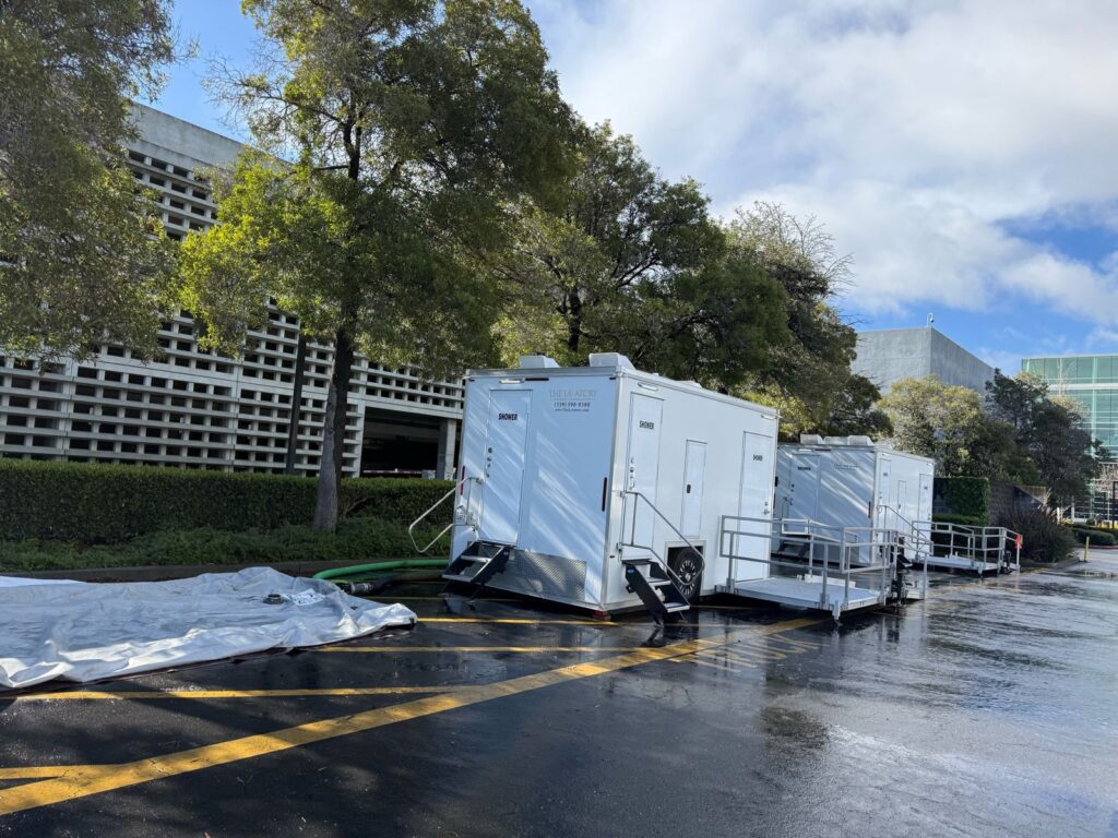 Two private shower trailers with steps and ramps lined up in an office campus parking lot after rain, The Lavatory Los Angeles