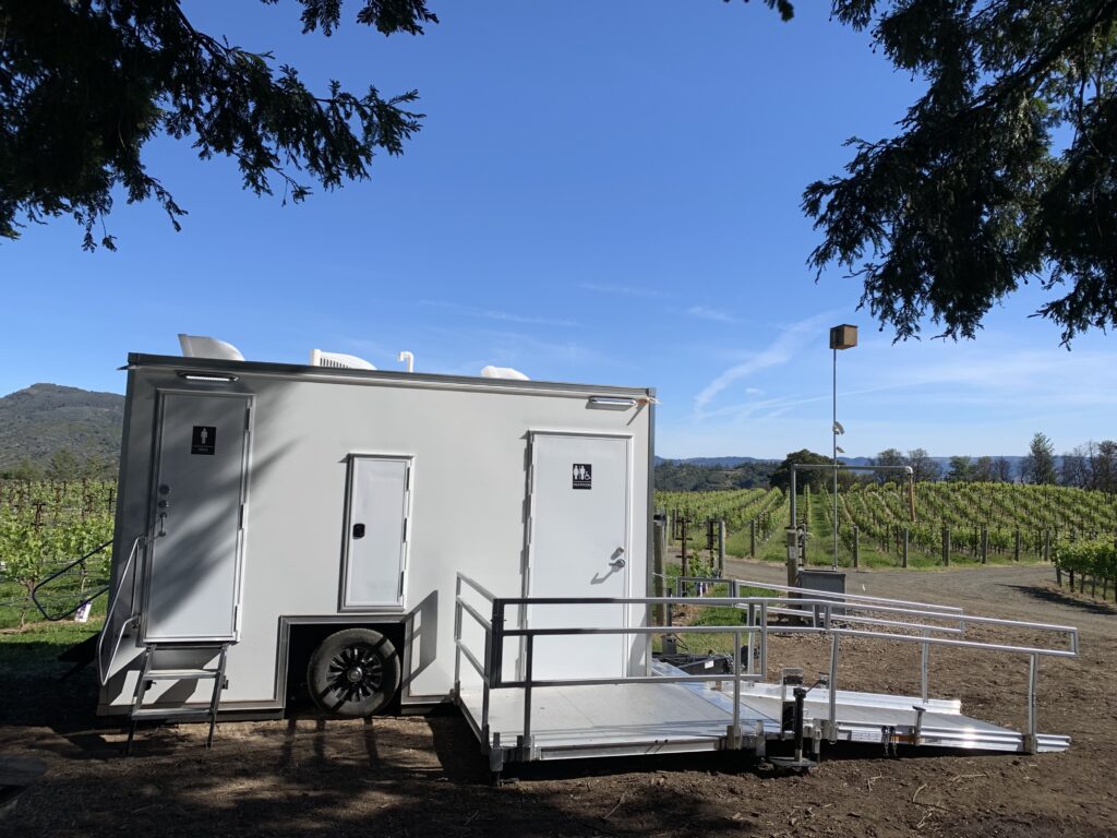 ADA plus 2 bathroom trailer with a ramp with handrails set up beside a vineyard for a private event, The Lavatory Los Angeles