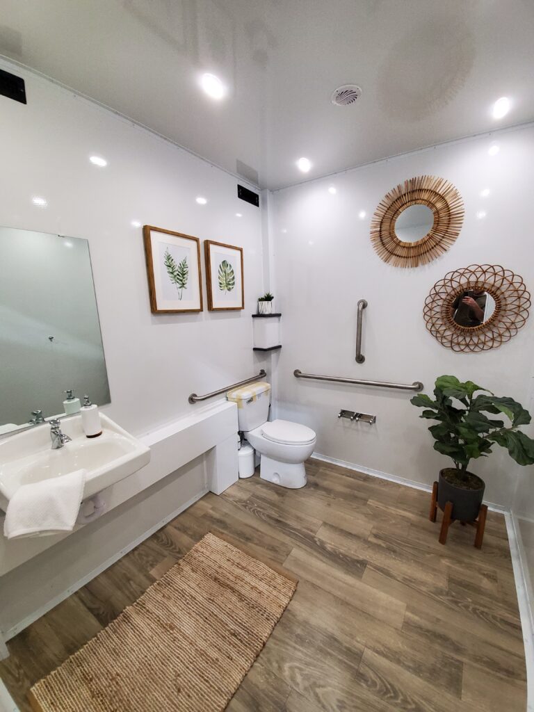 Accessible bathroom trailer interior with grab bars, toilet, sink and woven rug, The Lavatory Los Angeles