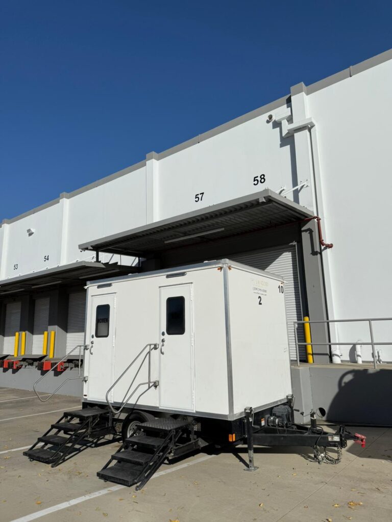 2-station bathroom trailer parked by the loading docks of a distribution warehouse for its workers on a long-term rental, The Lavatory Los Angeles