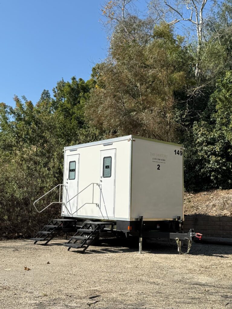 2-station bathroom trailer with steps and rails set on gravel under trees for a film crew on a park shoot, The Lavatory Los Angeles