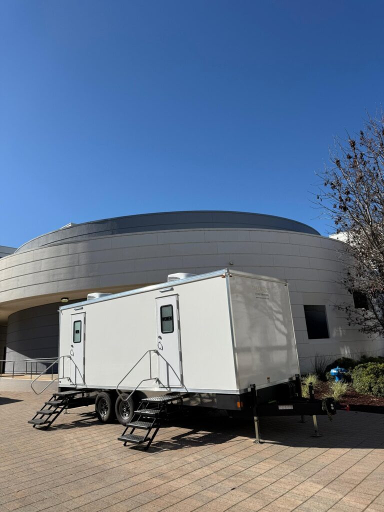 9-station bathroom trailer with fold-down steps parked on pavers beside a curved modern building, The Lavatory Los Angeles