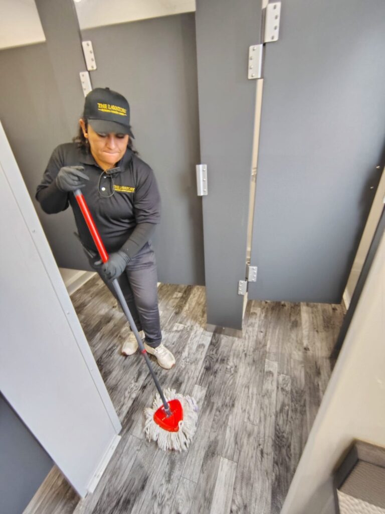 Attendant from our team in gloves mopping the floor between stalls inside a bathroom trailer, The Lavatory Los Angeles