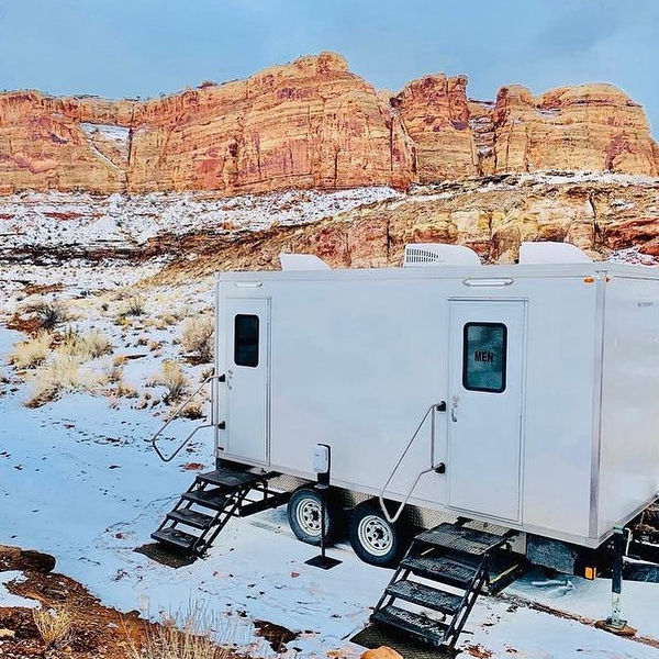 Bathroom trailer with steps set on snowy ground below red rock cliffs, The Lavatory Los Angeles