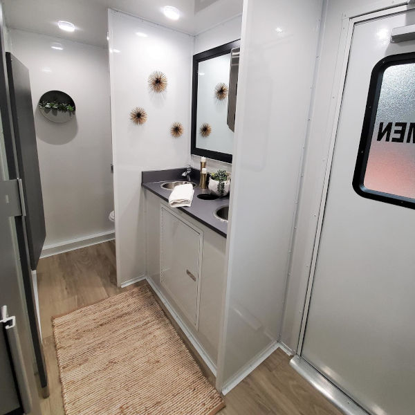 Vanity with dark countertop, black framed mirror and sunburst wall decor in a bathroom trailer, The Lavatory Los Angeles