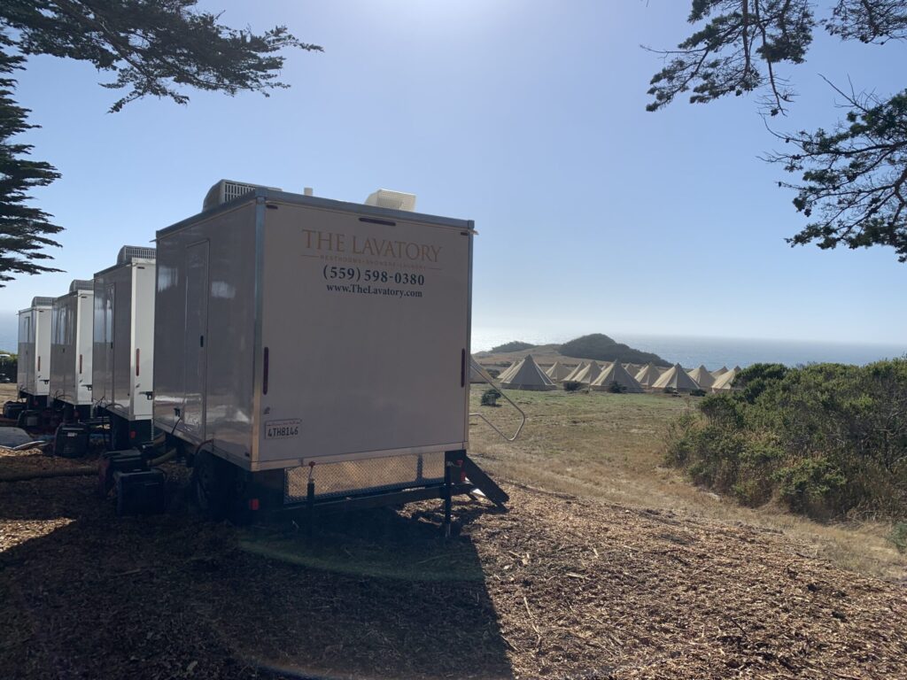 Row of bathroom trailers on a coastal hillside beside glamping tents and the ocean, The Lavatory Los Angeles