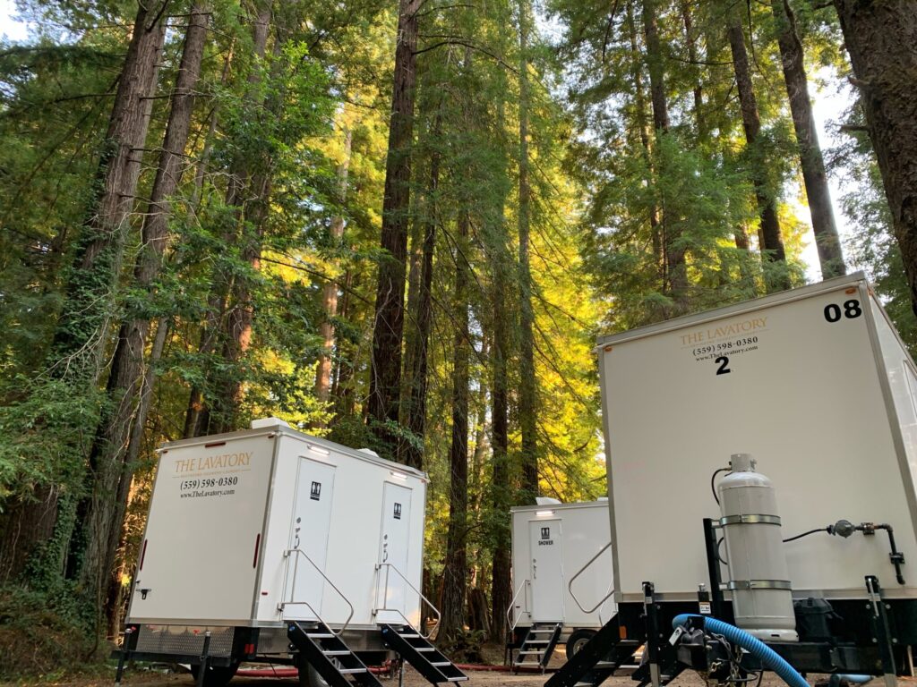 Bathroom and shower trailers set up among tall redwood trees at a forest camp, The Lavatory Los Angeles