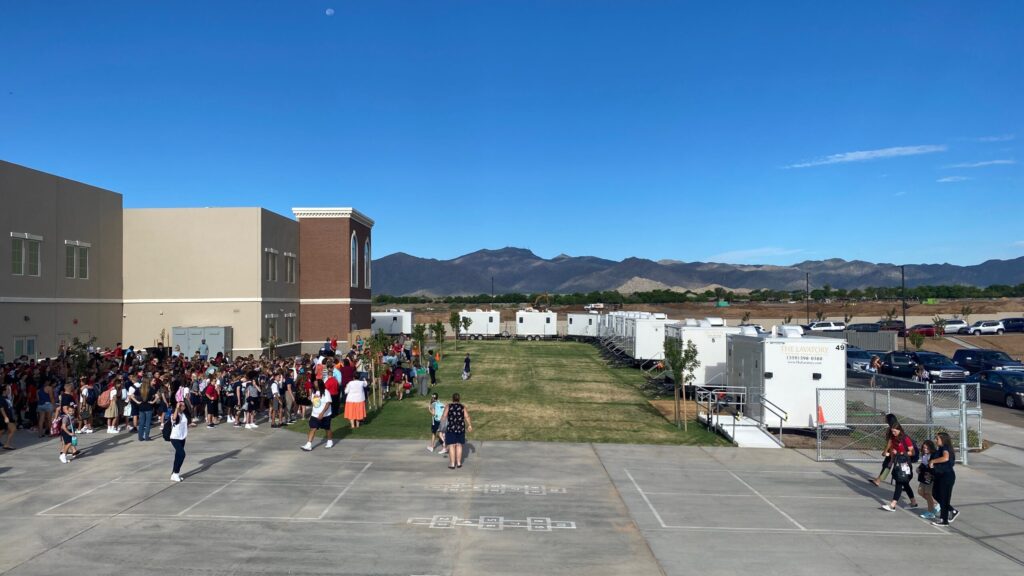 Row of bathroom trailers along a school campus field with crowds of students, The Lavatory Los Angeles