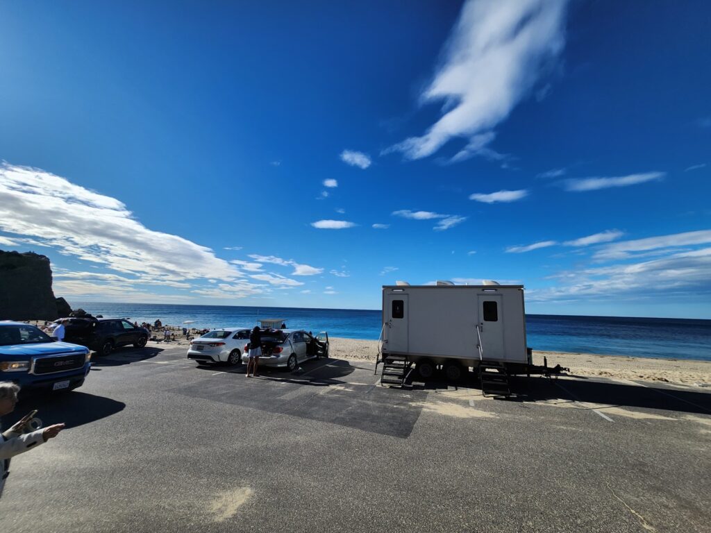 2-station combo shower trailer parked by the ocean at a beach parking lot with beachgoers nearby, The Lavatory Los Angeles
