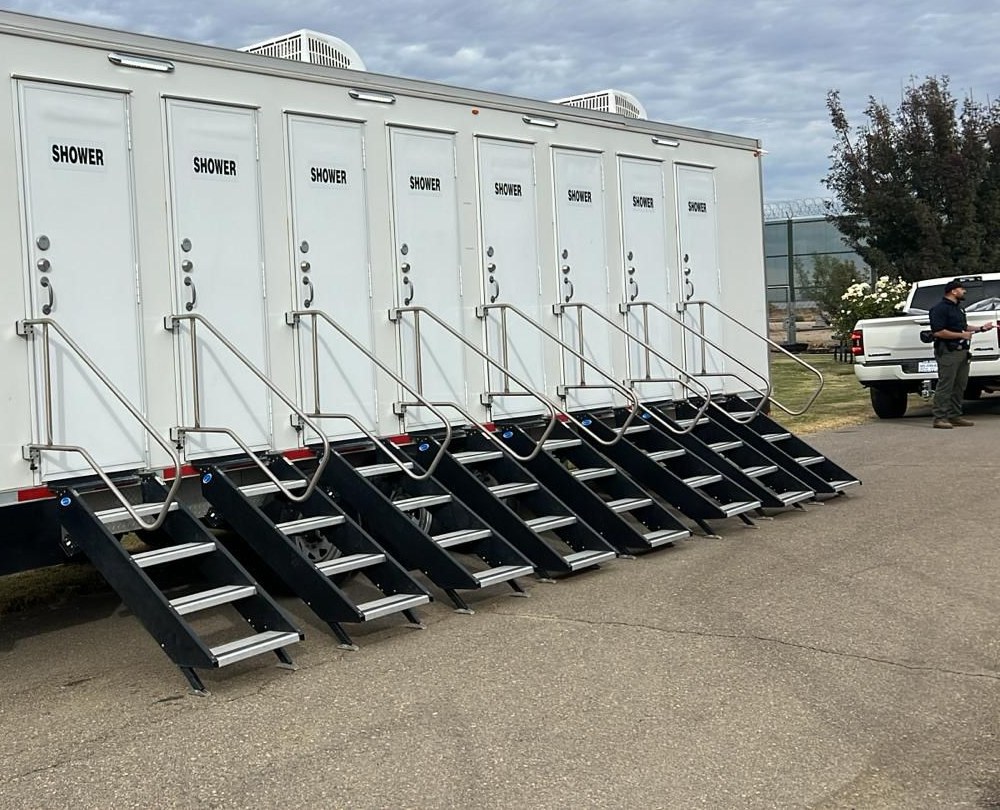 8-station private shower trailer with steps at every door and a staff member beside the delivery truck, The Lavatory Los Angeles