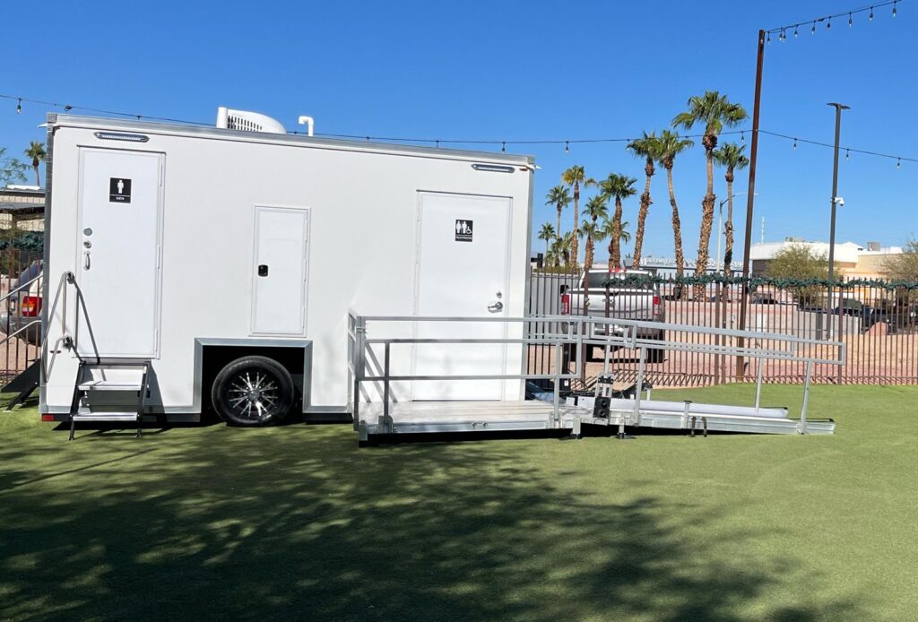 Accessible bathroom trailer with a railed ramp set on an event lawn under string lights and palm trees, The Lavatory Los Angeles