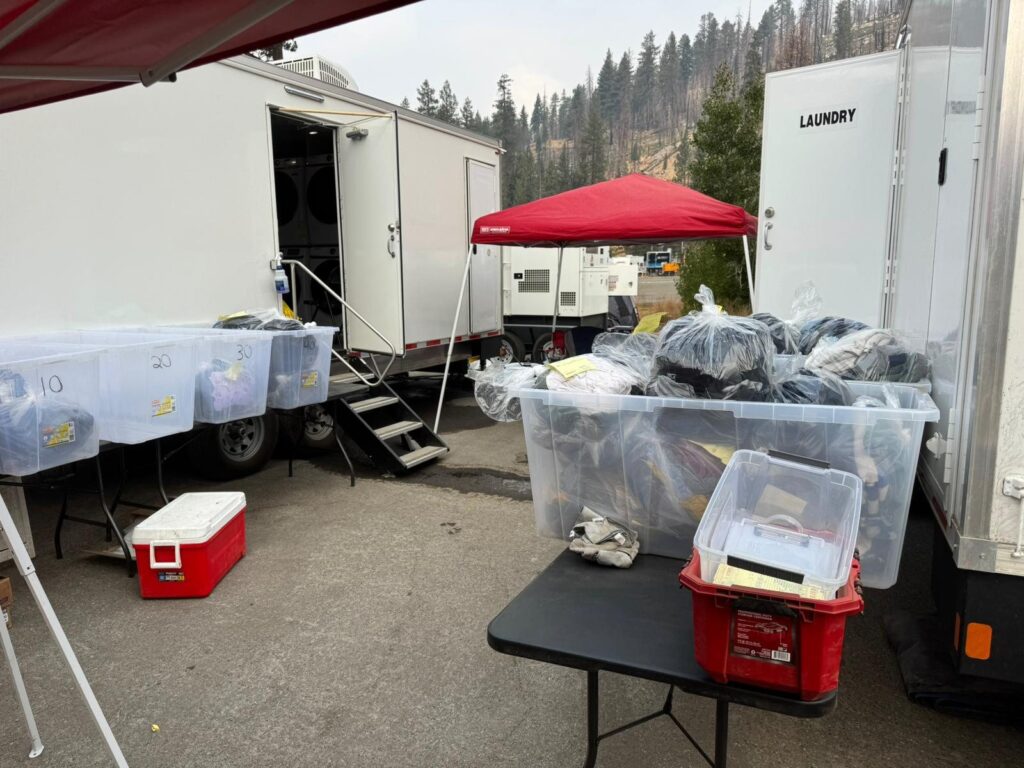 Numbered bins of bagged clean laundry outside an open mobile laundry trailer at a fire camp, The Lavatory Los Angeles