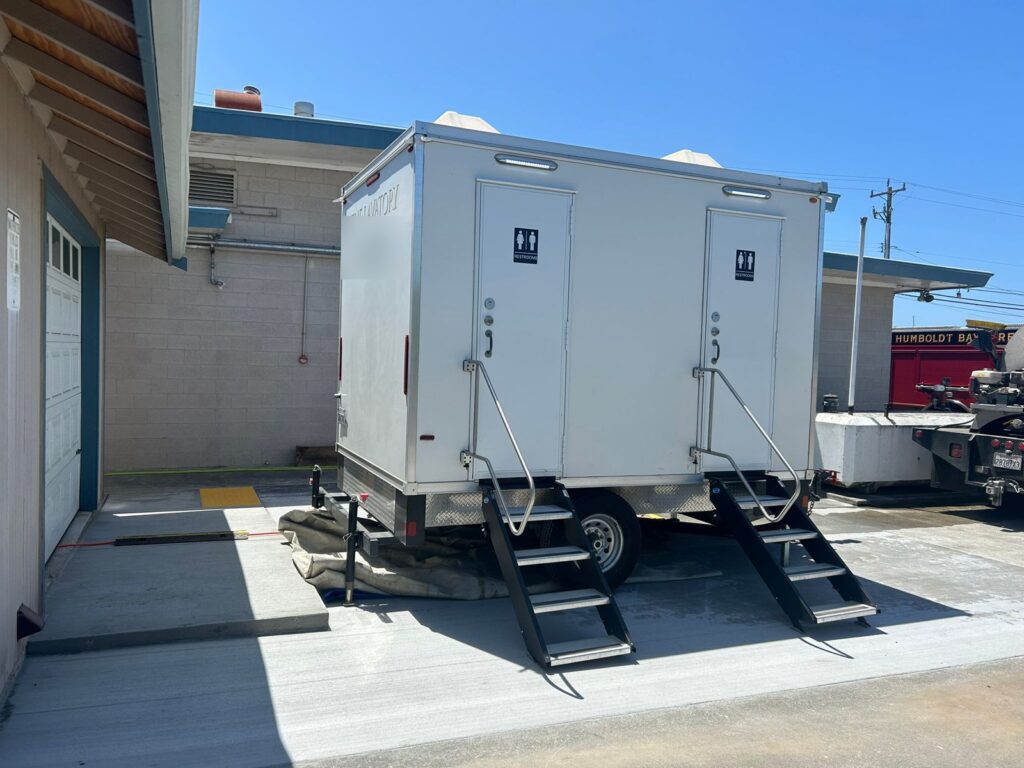 2-station bathroom trailer with two sets of fold-down steps parked in a fire station yard next to a fire engine, The Lavatory Los Angeles