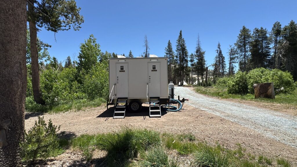 2-station combo trailer with a water hose hookup at a forest camp beside a gravel road, The Lavatory Los Angeles