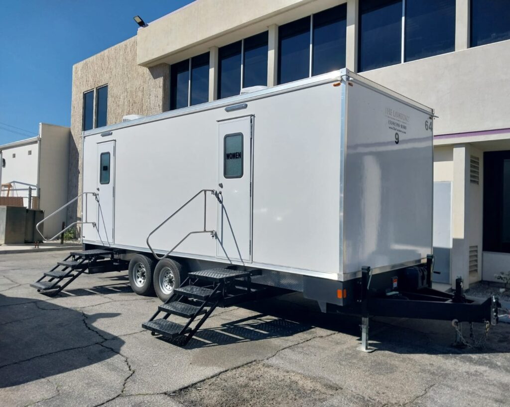 9-station deluxe bathroom trailer with entry steps parked beside a two-story office building, The Lavatory Los Angeles