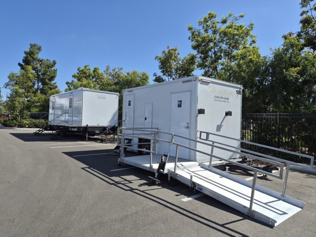 ADA bathroom trailer with a wheelchair ramp and a second bathroom trailer set up in a paved parking lot, The Lavatory Los Angeles