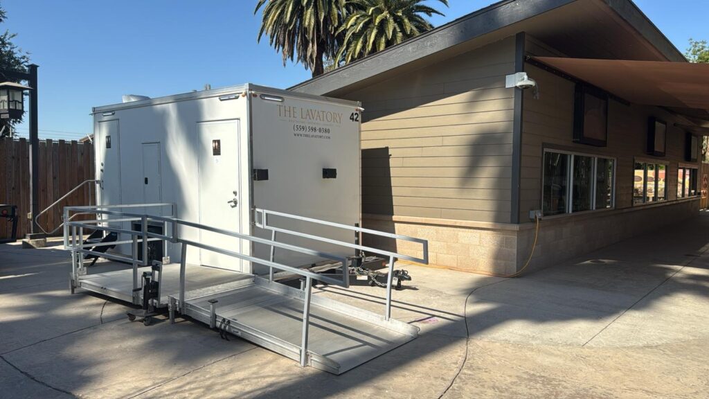 ADA plus 2 bathroom trailer with a railed wheelchair ramp set beside a building under palm trees, The Lavatory Los Angeles