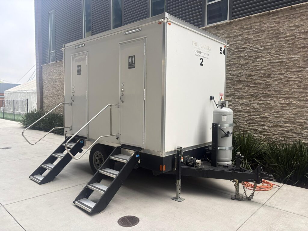 2-station bathroom trailer with two doors and steps beside a modern stone office building, The Lavatory Los Angeles