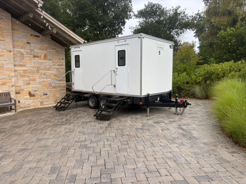 5-station bathroom trailer on a paver courtyard beside a stone event building, The Lavatory Los Angeles