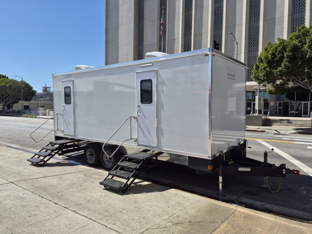 Bathroom trailer with fold-down steps parked at the curb in front of a civic office tower, The Lavatory Los Angeles
