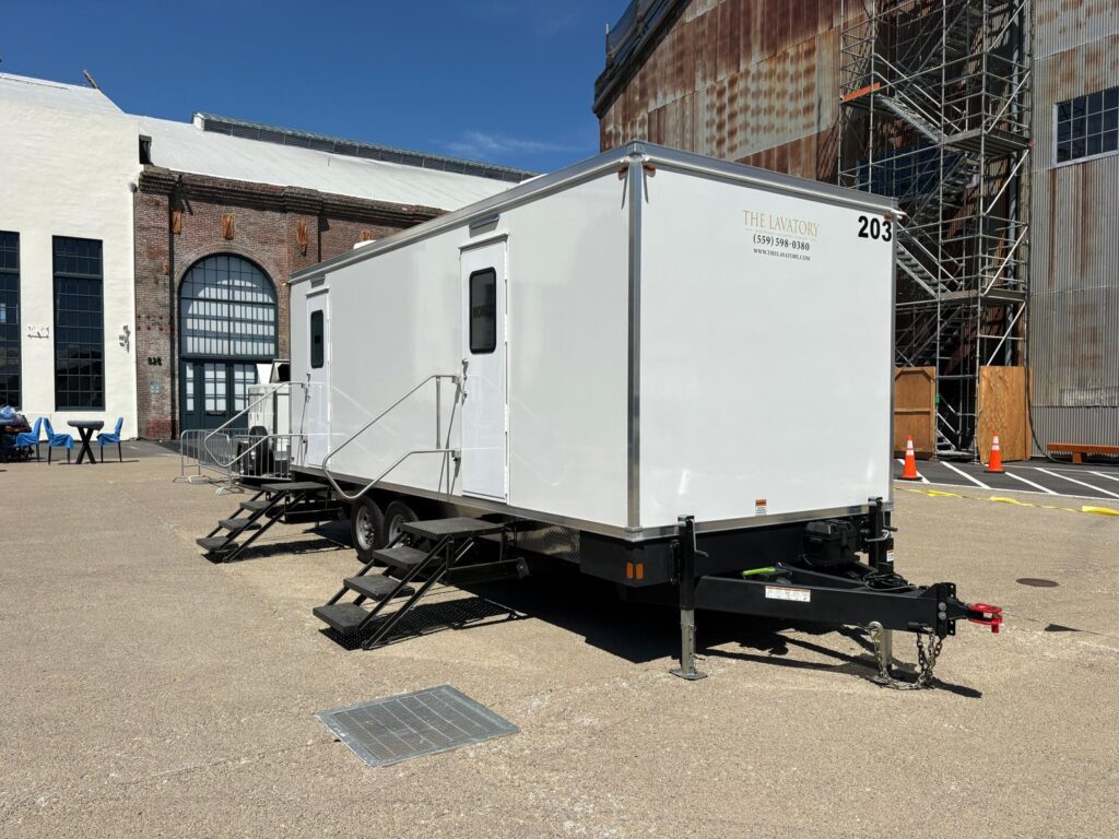 Bathroom trailer parked beside a historic brick building under renovation with scaffolding, The Lavatory Los Angeles