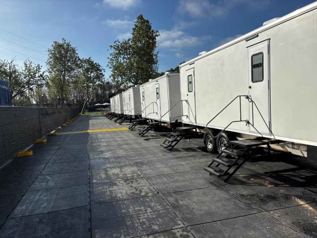 Long row of bathroom trailers set on ground mats along a fence line for a large event, The Lavatory Los Angeles
