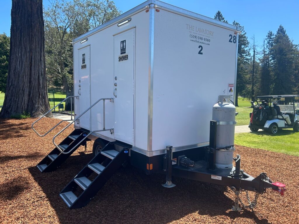 2-station combo trailer on wood chips beside a golf course fairway and a golf cart, The Lavatory Los Angeles