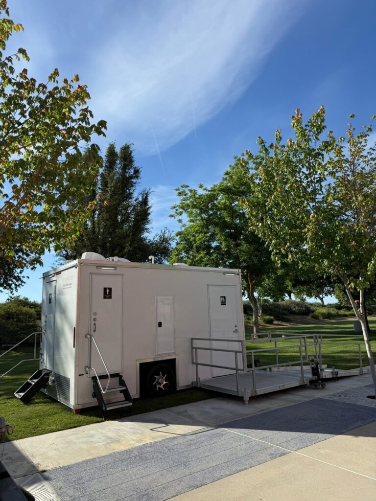 Two bathroom trailers with steps and a ramp landing set on a hospital campus lawn, The Lavatory Los Angeles