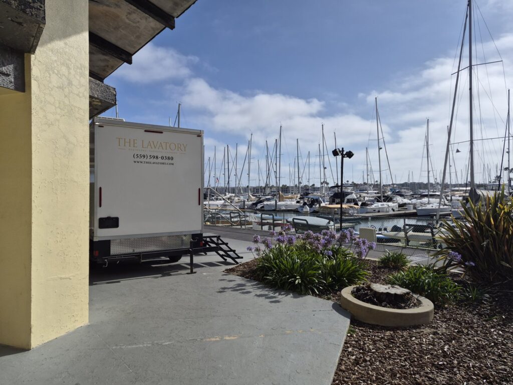 2-station bathroom trailer parked on a walkway next to a sailboat marina, The Lavatory Los Angeles