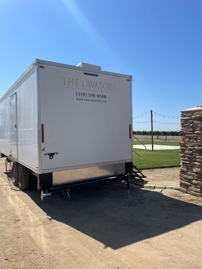 9-station bathroom trailer beside a stone pillar and a lawn strung with party lights, The Lavatory Los Angeles