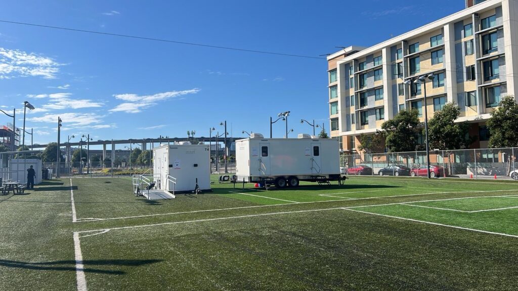 ADA trailer with a ramp and a 9-station bathroom trailer set up on an artificial turf sports field, The Lavatory Los Angeles