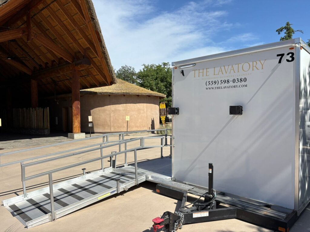 ADA bathroom trailer with a railed ramp set beside a timber event pavilion, The Lavatory Los Angeles