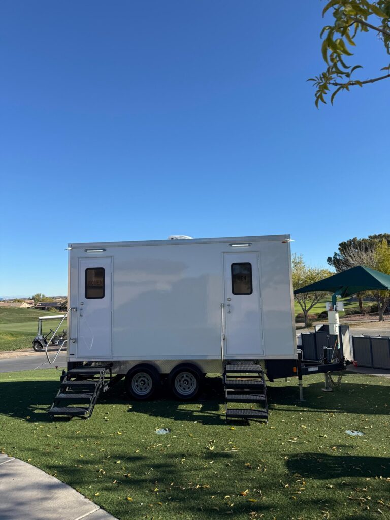 Bathroom trailer with women's and men's doors set up on turf beside a golf course, The Lavatory Los Angeles