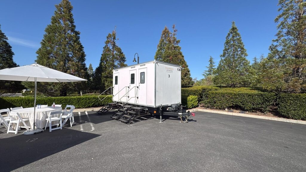 3-station bathroom trailer parked beside a white party table and umbrella at a private estate, The Lavatory Los Angeles
