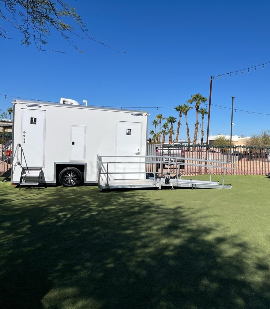 Accessible bathroom trailer with a long railed ramp on an event lawn under string lights and palm trees, The Lavatory Los Angeles
