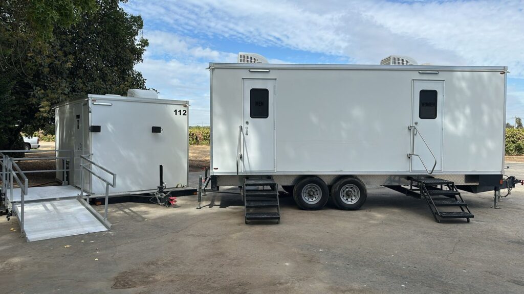 Accessible bathroom trailer with a ramp parked beside a 9-station bathroom trailer on a dirt lot, The Lavatory Los Angeles