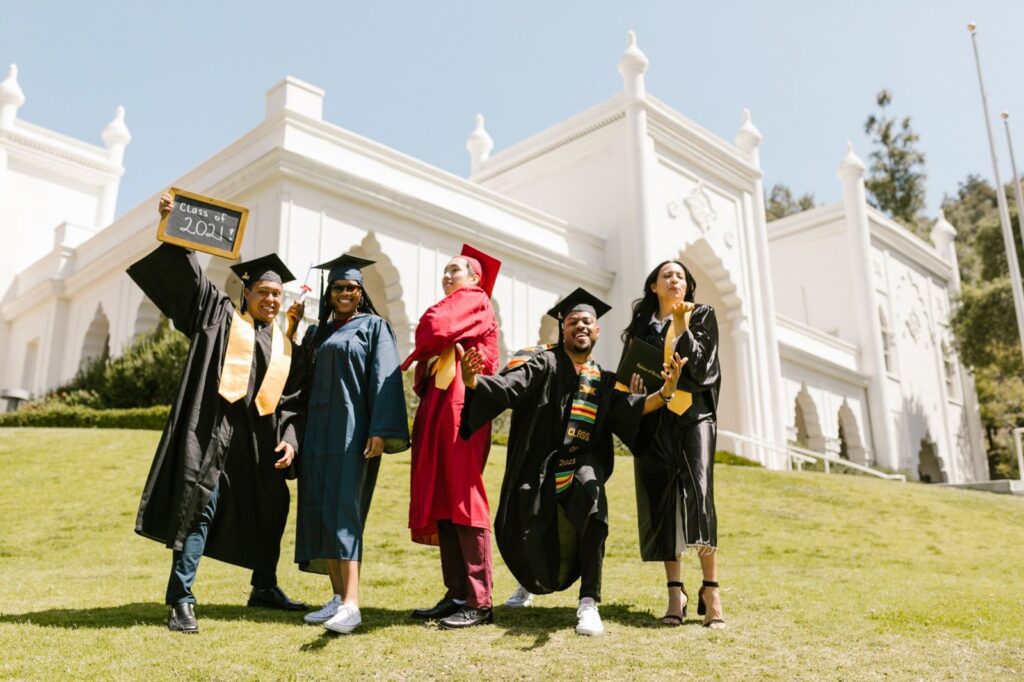 Graduates in caps and gowns celebrating on a campus lawn, The Lavatory Los Angeles