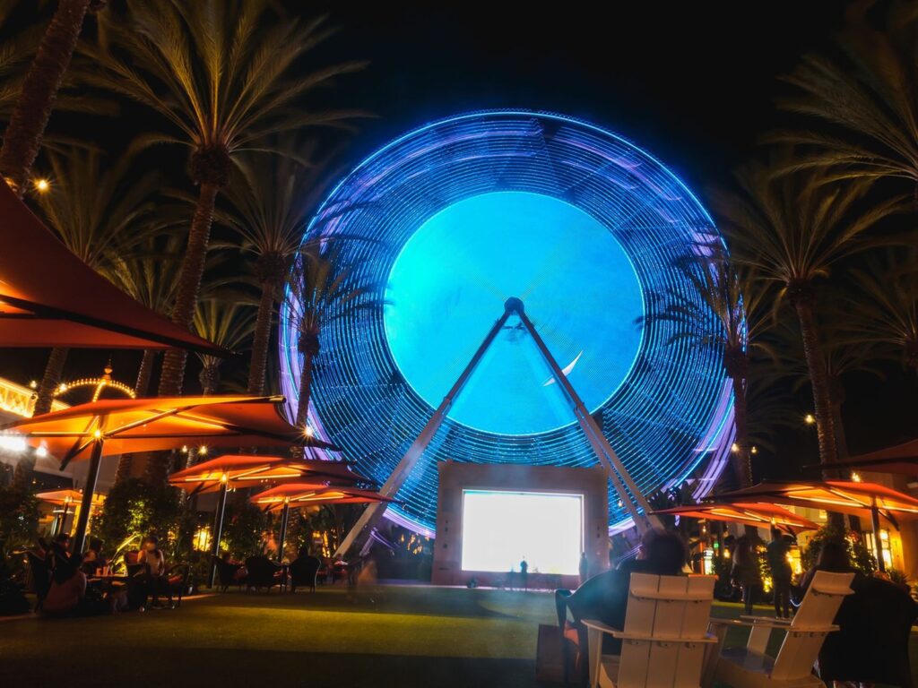 People relaxing under the lit Ferris wheel and palm trees at Irvine Spectrum Center at night in Irvine, CA, The Lavatory Los Angeles