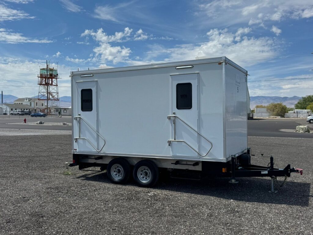 5-station bathroom trailer on a gravel pad at an airfield with an old control tower behind it, The Lavatory Los Angeles
