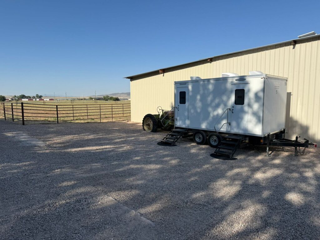 5-station bathroom trailer on gravel beside a metal building with open fields and hills beyond, The Lavatory Los Angeles