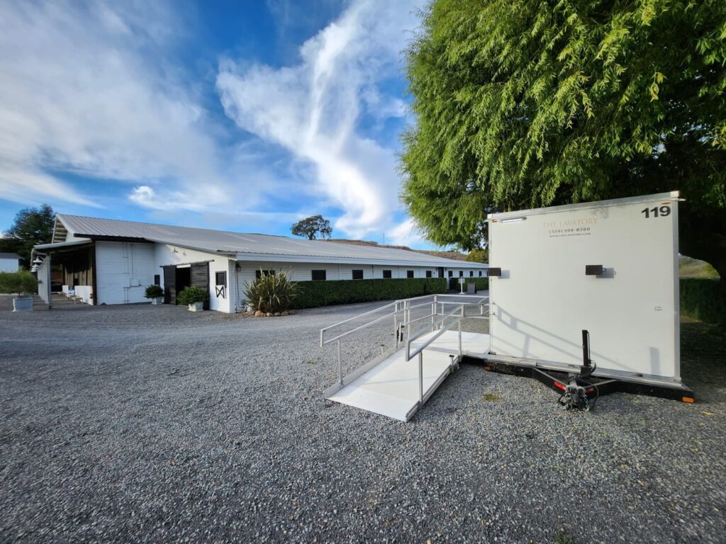 Accessible bathroom trailer with a long ramp on a gravel drive next to a horse stable, The Lavatory Los Angeles