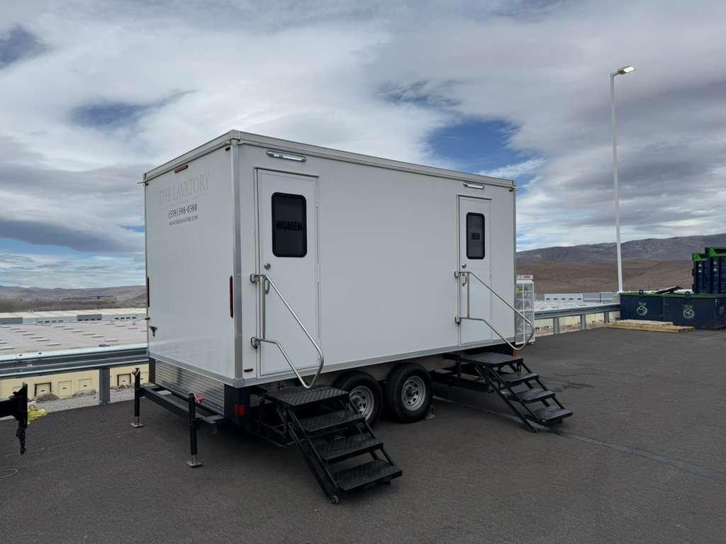 Bathroom trailer with two doors on a paved jobsite pad with desert mountains in the distance, The Lavatory Los Angeles