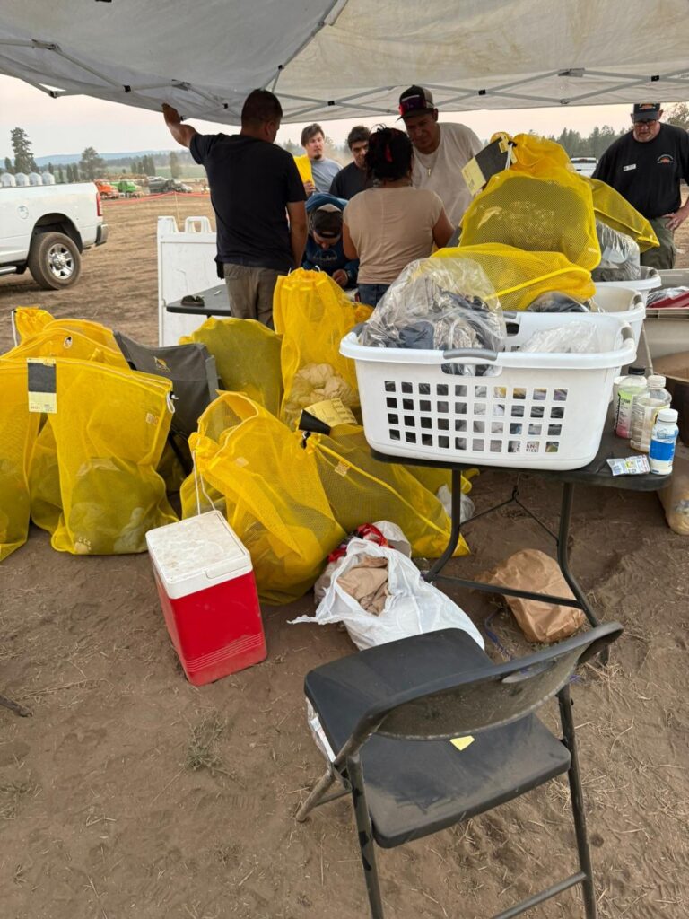 Camp workers sorting yellow laundry bags and baskets at a drop-off table under a canopy, The Lavatory Los Angeles