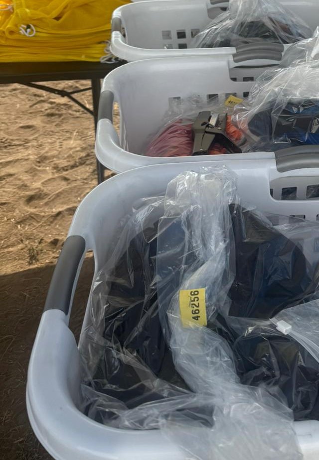 Laundry baskets of bagged clothes with numbered tags waiting at a camp drop-off table, The Lavatory Los Angeles