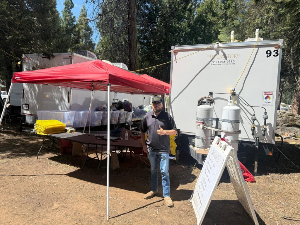 Staff member giving a thumbs up at the laundry tent beside a mobile laundry trailer at a camp, The Lavatory Los Angeles